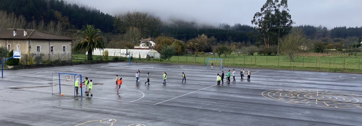 Foto panorámica de patio de ikastola donde una clase de primaria juega a quidditch